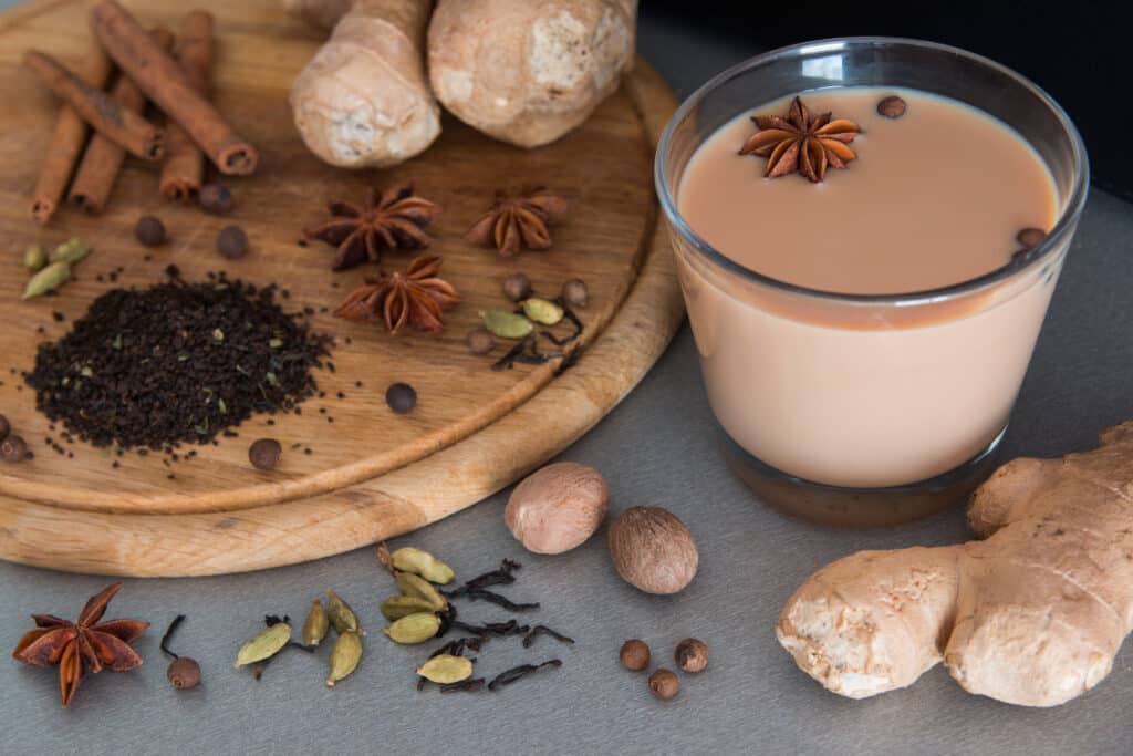 Aromatic Indian chai in Melbourne served in a glass with whole spices like star anise, cardamom, cinnamon, and ginger on a wooden board.